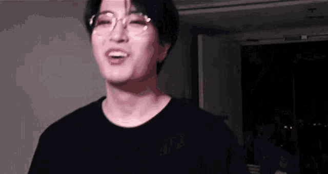 a young man wearing glasses and a black shirt is laughing .