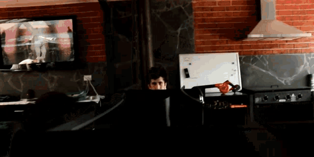 a man is sitting in front of a television with a brick wall behind him