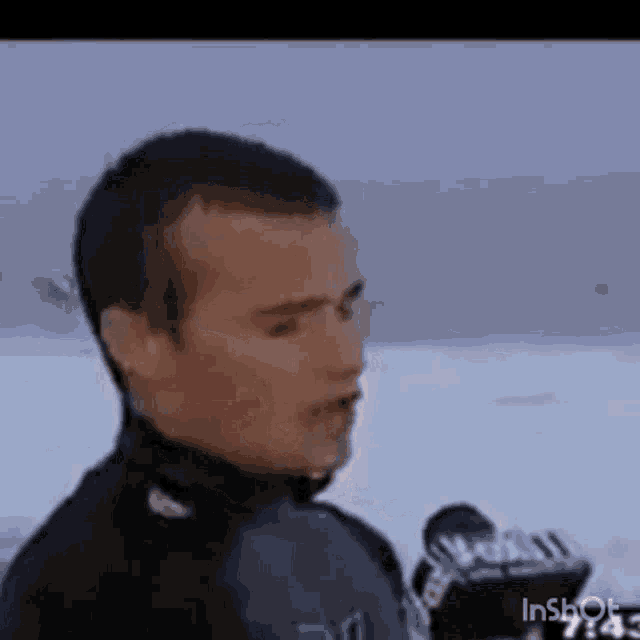 a man in a wet suit is talking into a microphone on a beach .