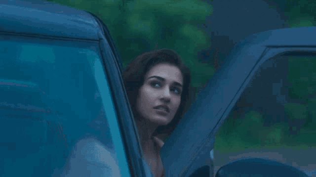 a woman in a white dress looks out of a blue car window