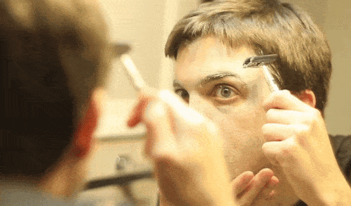 a man shaves his eyebrows in front of the mirror