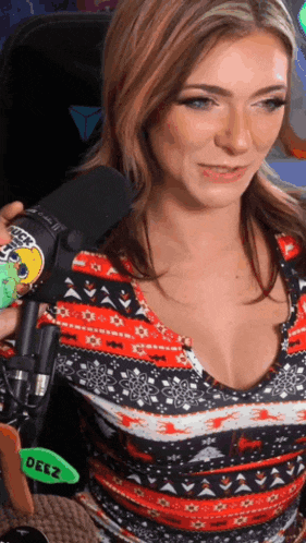 a woman in a sweater is sitting in front of a microphone and holding a sticker that says deez .