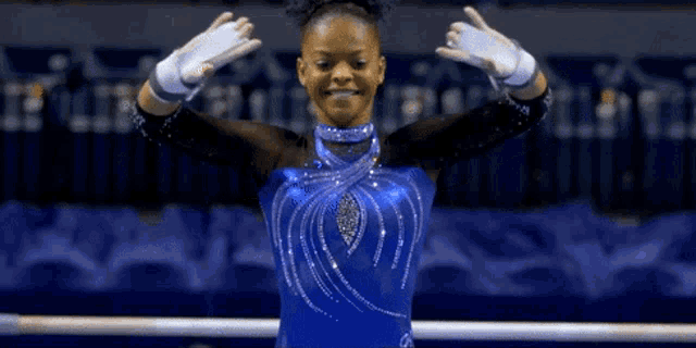 a female gymnast in a blue leotard is standing on a bar
