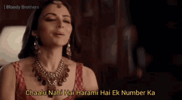 a woman wearing a red top and a necklace with the words chaalu nahi hai harami hai ek number ka