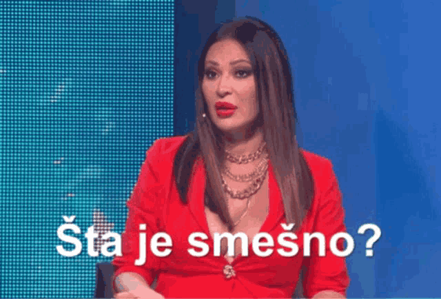a woman in a red dress is sitting in front of a screen that says " sta je smešno " .