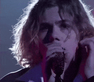 a man with long hair singing into a microphone