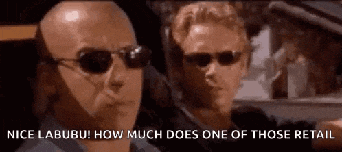 two men wearing sunglasses are driving a car and one of them is talking to the other .
