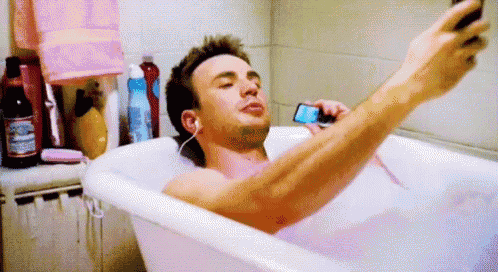 a man is taking a selfie in a bathtub while listening to music on a cell phone .