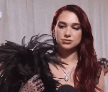 a woman with red hair is wearing a black feathered jacket and necklace .