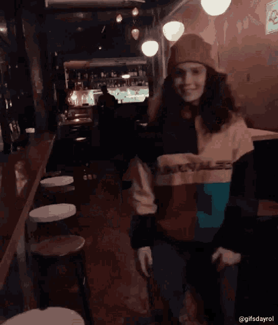 a woman in a colorful sweater and hat is sitting on a stool in a restaurant .