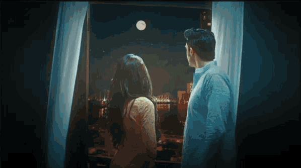 a man and woman looking out a window at the moon