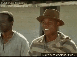 two men are standing next to each other and one of them is wearing a hat and striped shirt .