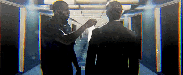 two men are standing next to each other in a hallway and one of them is holding a microphone .