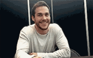 a man is smiling while sitting at a table with his arms crossed .