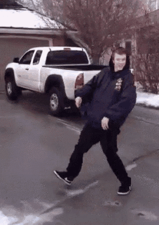 a man in a blue jacket is dancing in front of a white truck .