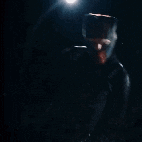 a man in a hooded jacket is holding a stack of money in his hands in the dark .