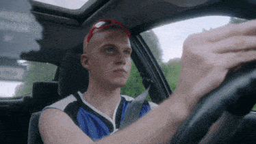 a man wearing sunglasses and a blue and white shirt is driving a car