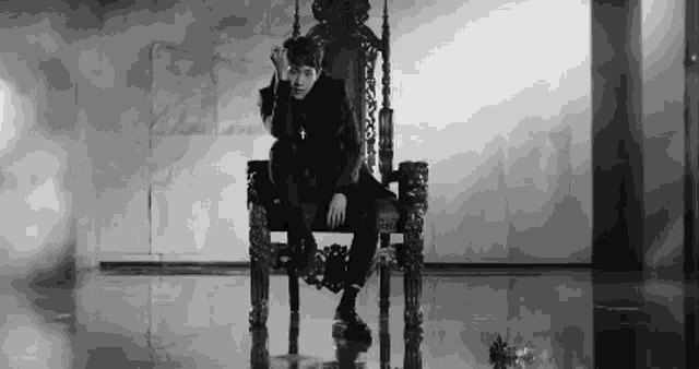 a black and white photo of a man sitting on a throne with a cross around his neck .