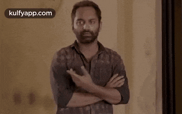a man with a beard is standing with his arms crossed and making a gesture .
