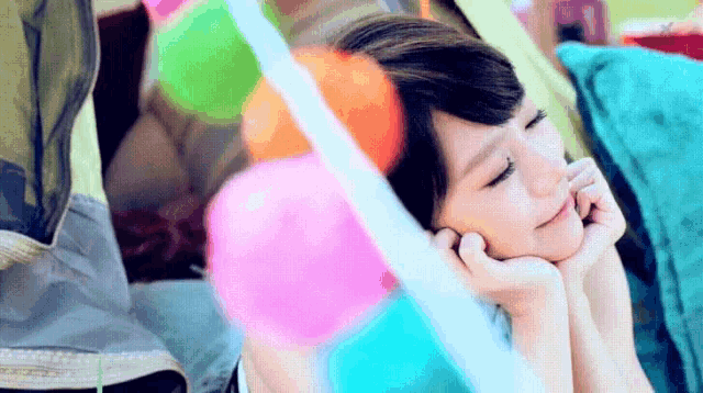 a woman is laying in a tent with her head resting on her hands surrounded by colorful balloons .