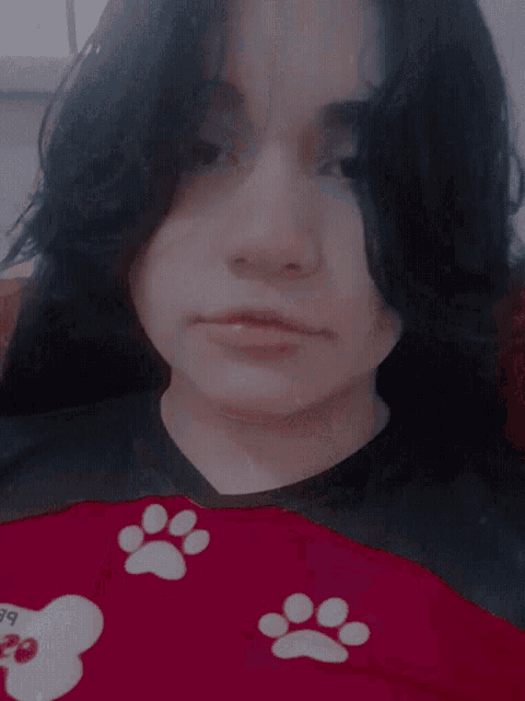 a woman wearing a red shirt with paw prints on it is giving a thumbs up