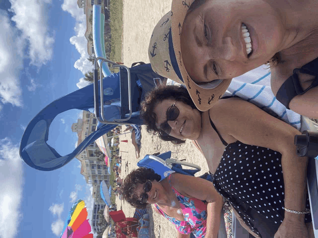 a woman wearing a hat with anchors on it sits on the beach with two other women