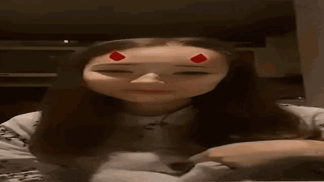 a woman with red devil horns on her forehead is making a heart with her fingers .
