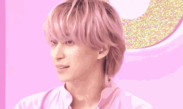 a young man with pink hair is wearing a pink shirt and earphones .