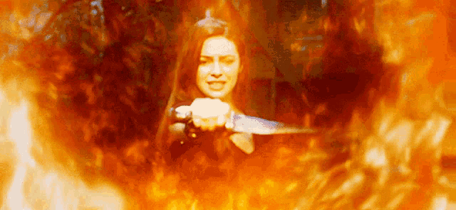 a woman is holding a sword in front of a fire background