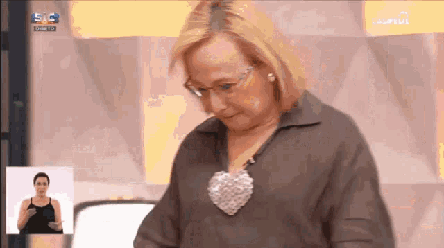 a woman wearing glasses and a heart shaped necklace on a tv screen