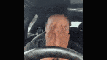 a man is covering his face with his hands while driving a car .