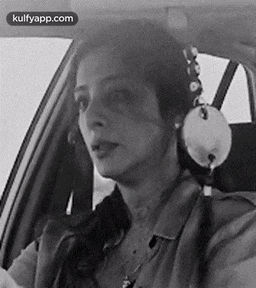 a black and white photo of a woman wearing headphones while sitting in a car .