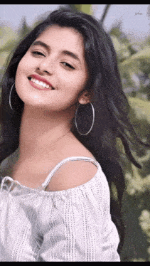 a young woman wearing hoop earrings and a white off the shoulder top smiles for the camera