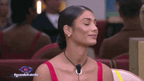 a woman in a red top is sitting in front of a sign that says #grandefratello