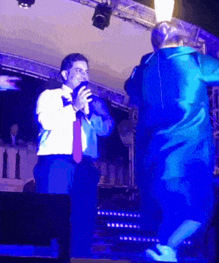 a man singing into a microphone with a woman in a blue dress dancing behind him