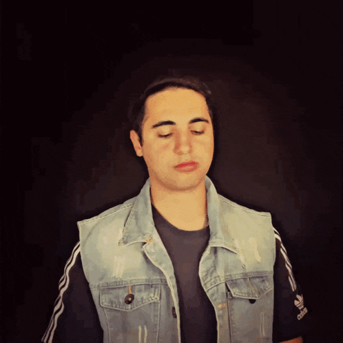 a man wearing a denim vest and a black shirt with adidas on the sleeve