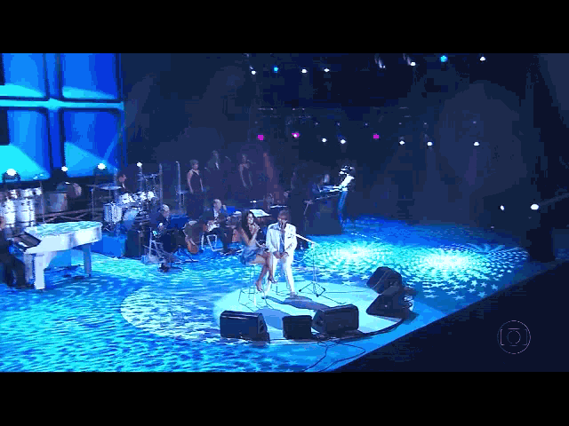 a man and woman singing on a stage with a piano