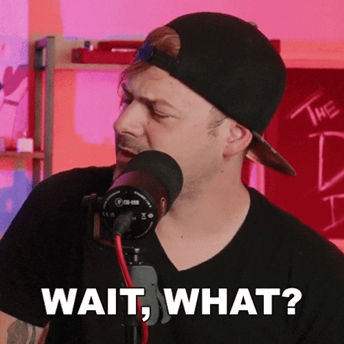 a man wearing a baseball cap and a black shirt is standing in front of a microphone and says wait what