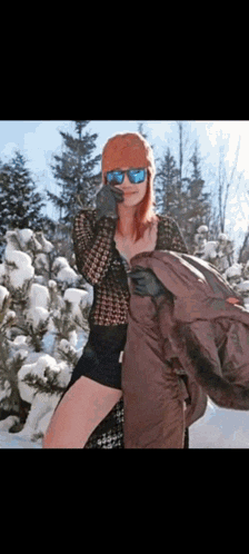 a woman wearing sunglasses and a beanie stands in the snow