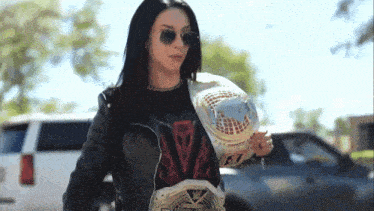 a woman wearing a t-shirt that says ' slayer ' on it is holding a wrestling championship belt