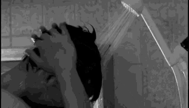 a black and white photo of a person taking a shower with their head in the shower head .
