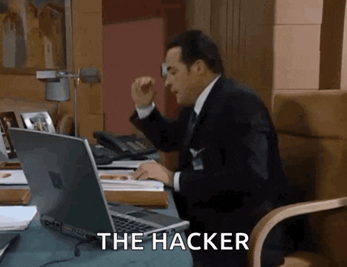 a man in a suit and tie is sitting at a desk with a laptop and the words the hacker behind him
