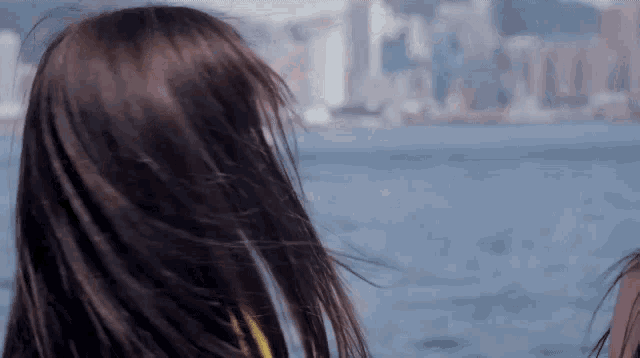 a woman 's hair is blowing in the wind while looking at the ocean .