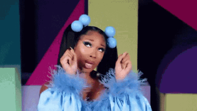 a woman in a blue dress and feathered cuffs is making a heart shape with her hands .