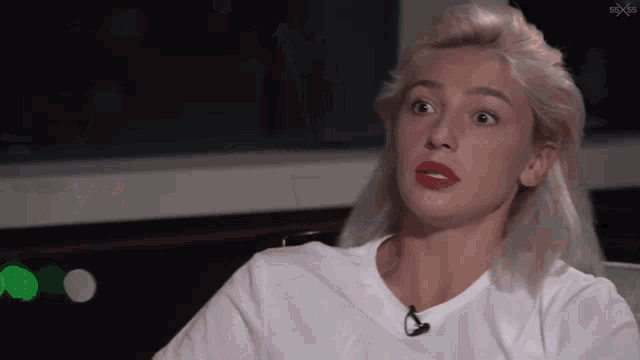 a woman with blonde hair and red lipstick is wearing a white t-shirt and sitting in a chair .