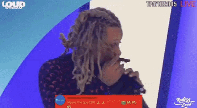 a man with dreadlocks is singing into a microphone in front of a loud stream sign