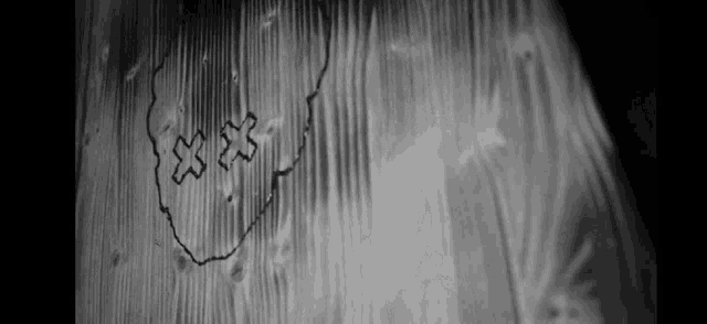 a black and white photo of a drawing of a face on a wooden wall .