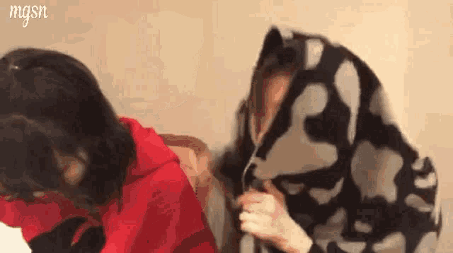 two women are covering their faces with a blanket and laughing .