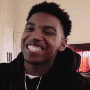 a young man in a black hoodie is smiling in a room .