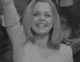 a black and white photo of a woman laughing with her hand in the air .